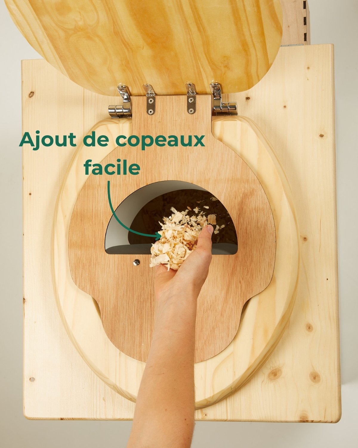 Main versant des copeaux de bois dans une toilette sèche à séparation à l’aide de la bavette intégrée à l’abattant